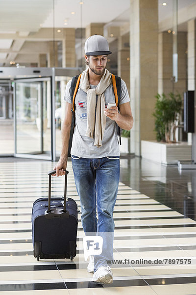 Mann  der sein Gepäck am Flughafen abzieht und ein Handy benutzt.