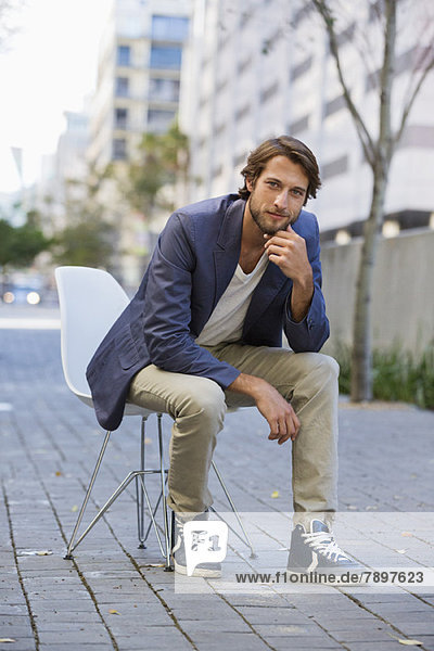 Porträt eines Mannes  der auf einem Stuhl auf einer Straße sitzt.