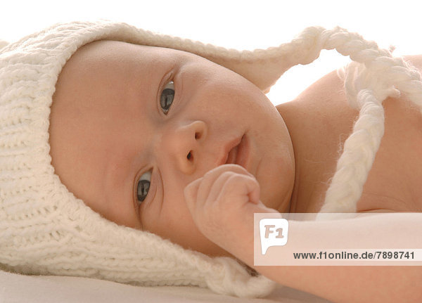 Säugling mit weißer Wollmütze  liegend  freier Oberkörper