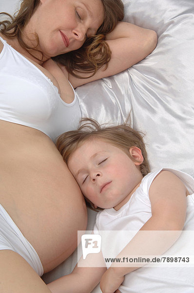 Junge liegt an Bauch von schwangerer Mutter  beide schlafen