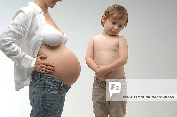 Schwangere Frau mit freiem Bauch steht neben Jungen mit nacktem Bauch