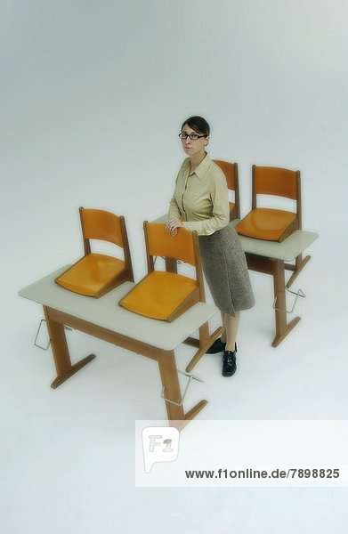 Strenge Lehrerin mit alten Schultischen und orangefarbenen Stühlen