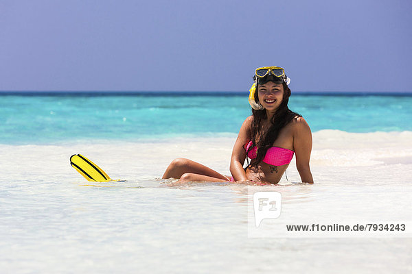 Junge Frau  etwa 20 Jahre  sitzt auf einer Sandbank  mit Schnorchelausrüstung