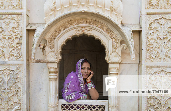 Junge freundliche Inderin mit Kopftuch schaut aus einer Fensteröffnung einer reich verzierten Marmorfassade  Rattentempel der Göttin Karni Mata  Karni-Mata-Tempel
