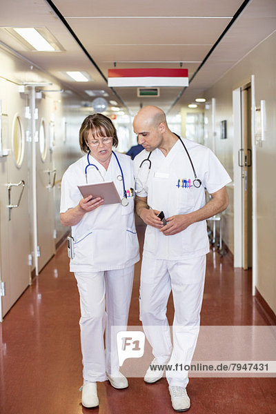 Male and female doctors using digital tablet while walking in hospital corridor