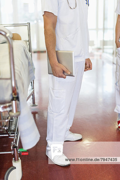 Niedriger Abschnitt des mittleren erwachsenen männlichen Arztes  der eine digitale Tablette hält  während er auf der Trage steht.