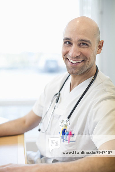 Porträt des glücklichen Arztes am Schreibtisch im Krankenhaus