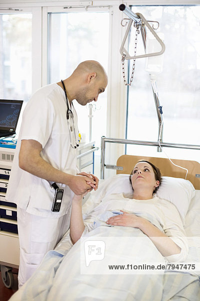 Male doctor consoling female patient lying on bed in hospital ward