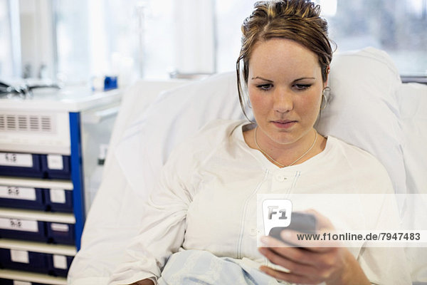 Mittlere erwachsene Patientin  die das Handy benutzt  während sie auf dem Bett in der Krankenstation liegt.