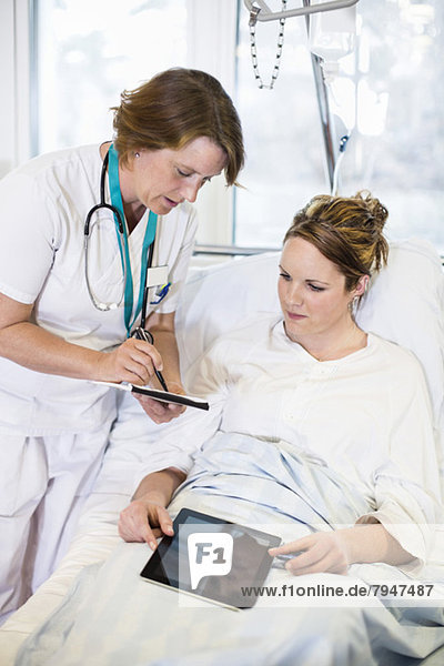 Female doctor showing notes to patient in hospital ward