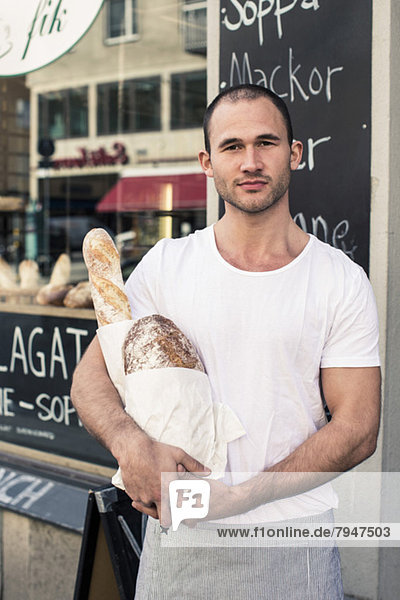 Porträt eines männlichen Besitzers mit Brotlaiben vor der Bäckerei