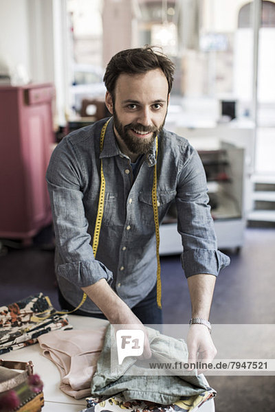 Porträt eines fröhlichen männlichen Designers  der am Tisch im Studio arbeitet.