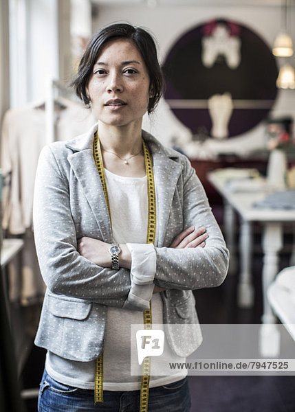 Porträt einer selbstbewussten Modedesignerin mit gekreuzten Armen im Atelier
