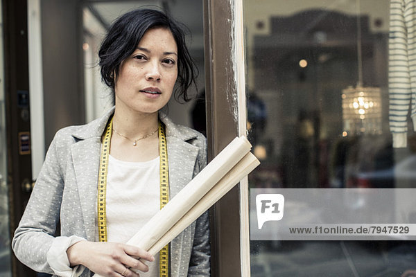 Portrait of female fashion designer holding blueprint while standing outside studio