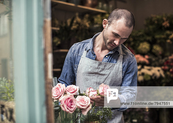 Mittlerer erwachsener männlicher Florist analysiert Blumen im Geschäft