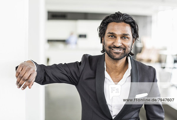 Portrait of mid adult businessman smiling while leaning on wall in office