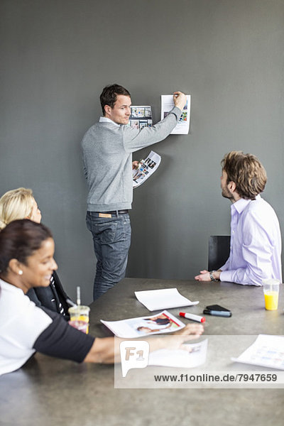 Mittlerer erwachsener Geschäftsmann  der ein Foto an die Wand klebt  während Kollegen ihn im Büro anschauen