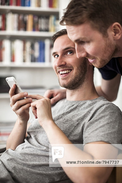 Happy young gay man looking at partner while using mobile phone at home