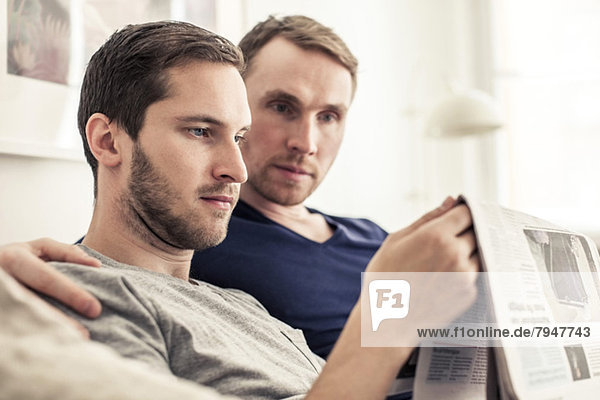 Homosexual couple reading newspaper together at home