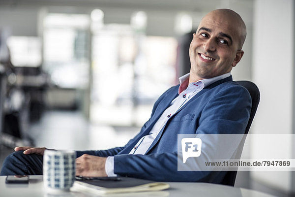 Mid adult businessman looking away while sitting at desk in office