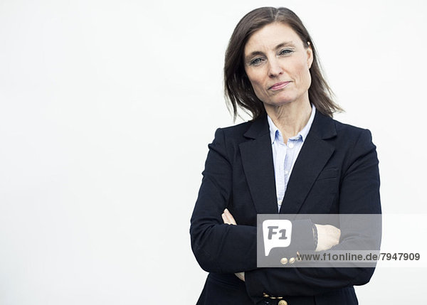 Portrait of confident mature businesswoman standing arms crossed against wall