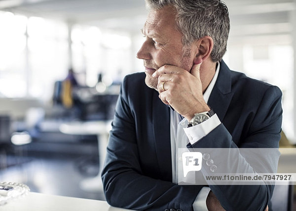 Thoughtful mature businessman looking away while sitting at desk in classroom