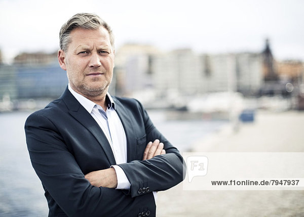 Portrait of confident mature businessman standing arms crossed by sea