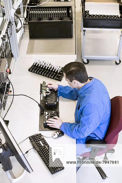 High angle view of mature male electrician working on machine part at desk in industry