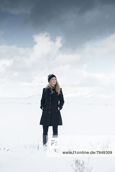 A young woman poses in hat and coat in the winter snow.