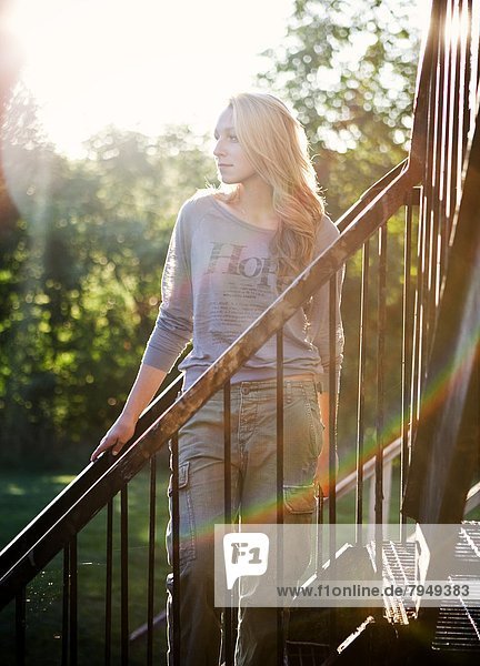 A young woman is illuminated by the late summer sun while posing for a portrait on a fire escape.