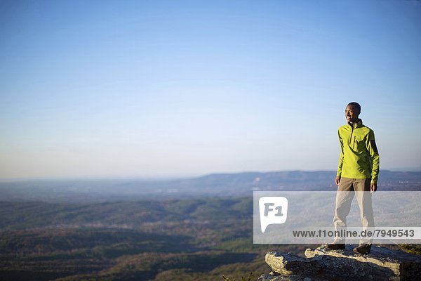 A young man smiles while standing on an boulder at the top of Cheaha Mountain.