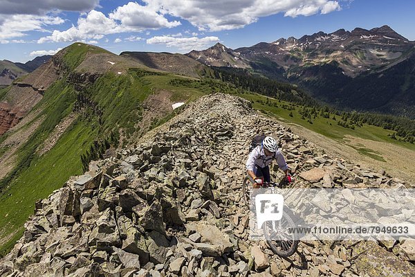 A mountain biker rides on a rocky trail through a talus field in the mountains.