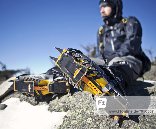 A mountaineer with crampons on rests on a rocky outcrop.
