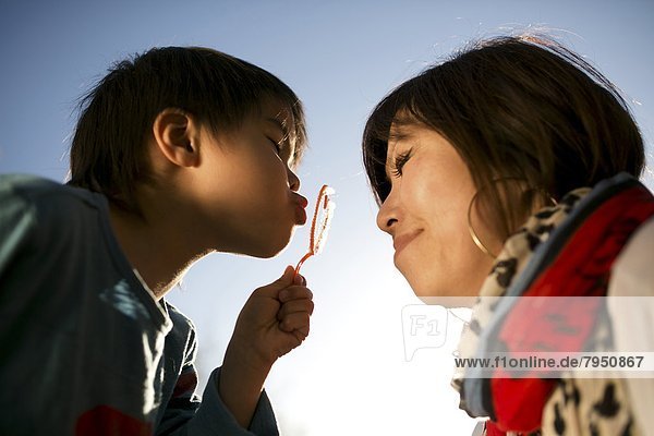 Young boy tries to blow a heart-shaped soap bubble for his mother.