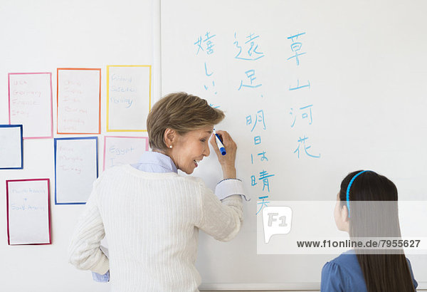 Teacher and schoolgirl (8-9) writing at whiteboard