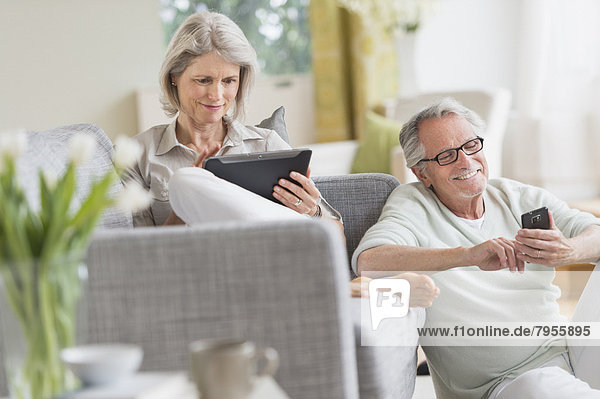 Senior couple using digital tablet and cell phone at home