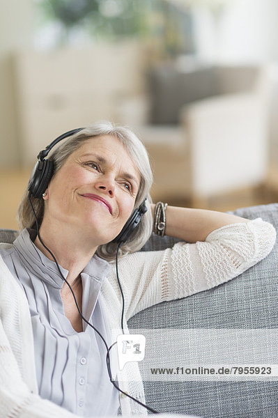 Senior woman sitting on sofa and listening to music