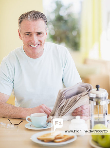 Portrait of man reading newspaper and having breakfast