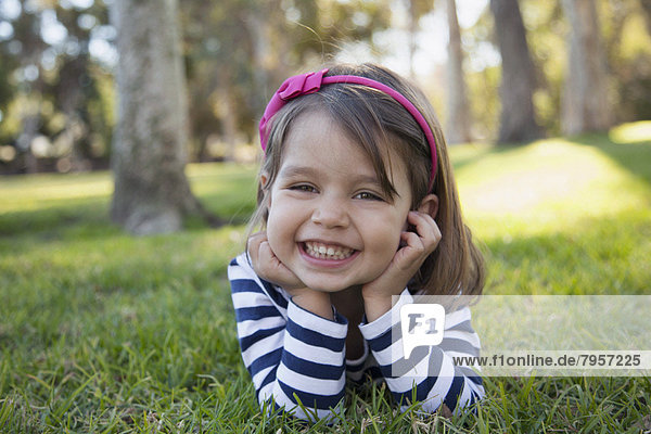 Portrait of smiling girl (4-5 years) lying on grass in park