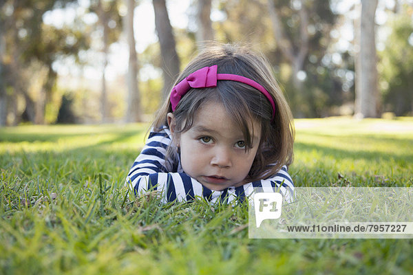Portrait of sad girl (4-5 years) lying on grass in park