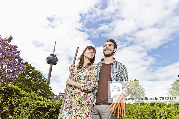 Deutschland  Köln  Junges Paar mit Karottenbüschel  lächelnd