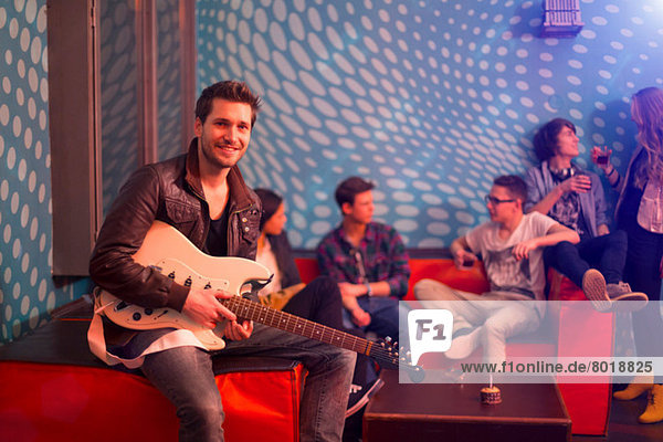 Mittlerer Erwachsener Mann mit Gitarre vor einer Gruppe von Teenagern sitzend