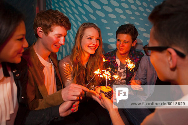 Gruppe von Teenagern sitzend um Geburtstagskuchen mit Wunderkerzen