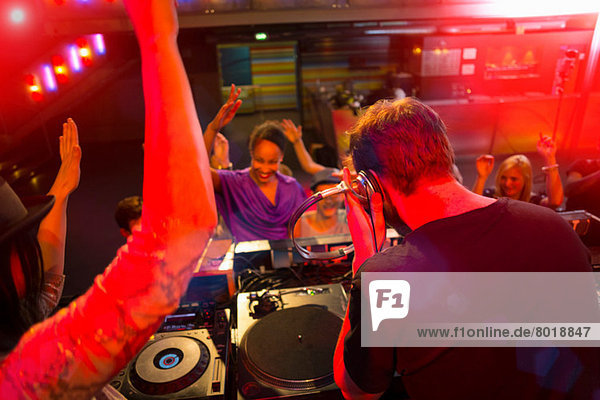 Rear view of disc jockey surrounded by people dancing