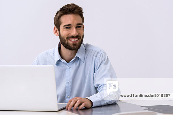 Portrait of young man sitting at desk with laptop