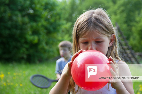 Nahes Porträt des jungen Mädchens beim Aufblasen des roten Ballons