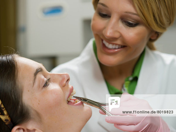 Zahnarzt mit Zahnzange an der Zahnspange einer jungen Frau