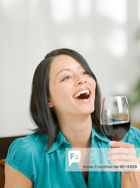 Reife Frau hält ein Glas Wein und lacht.