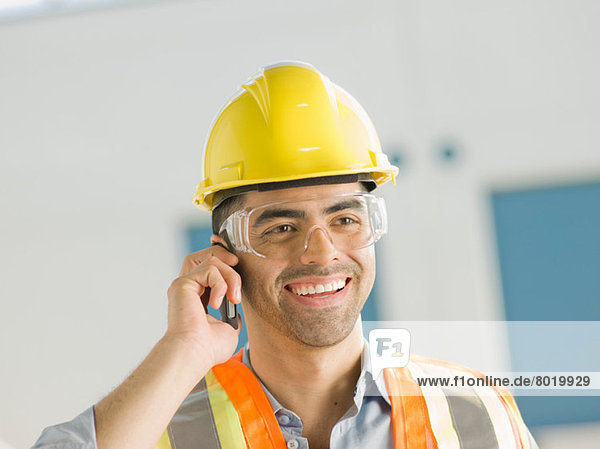 Mid adult construction worker using mobile phone  smiling