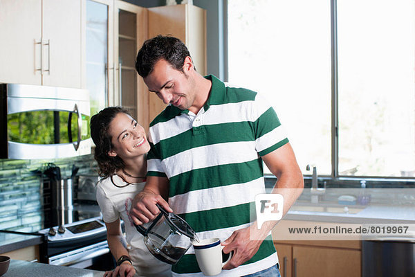 Junges Paar  das Kaffee aus der Kanne in die Küche gießt  lächelnd